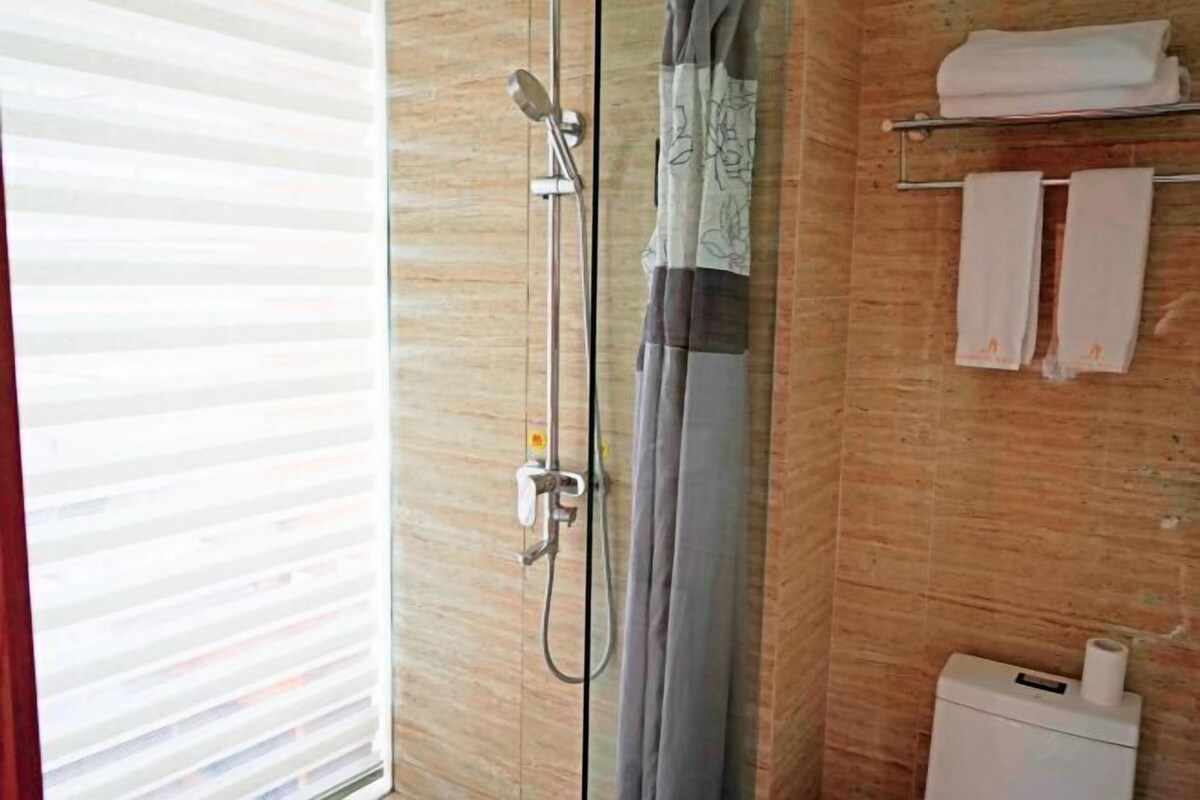 Et badeværelse med brusekabine i glas, et håndklædestativ med håndklæder og en toiletpapirholder.