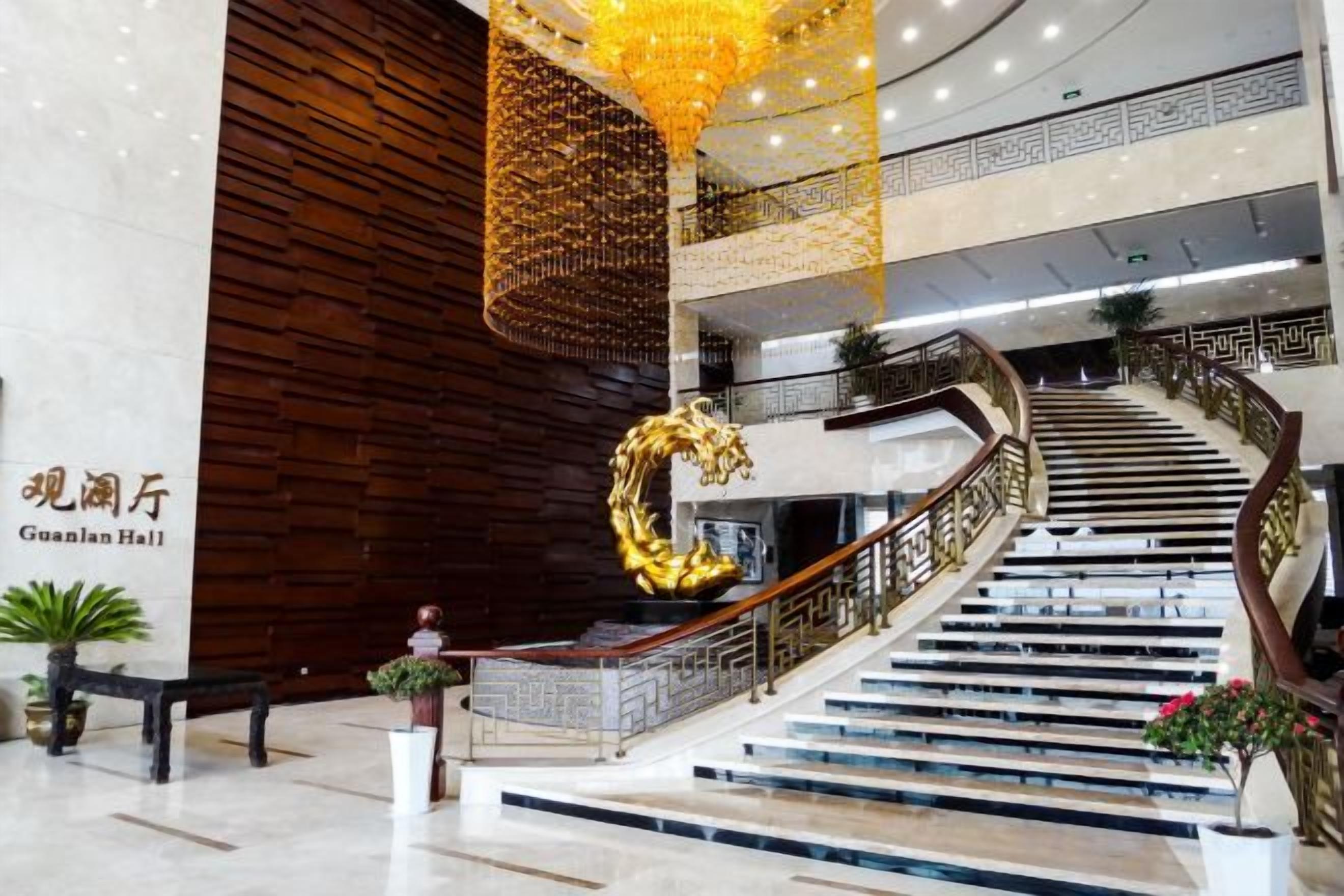 Un vestíbulo de hotel con una imponente escalera, una gran escultura dorada y un cartel que dice 'Guanjian Hall'.