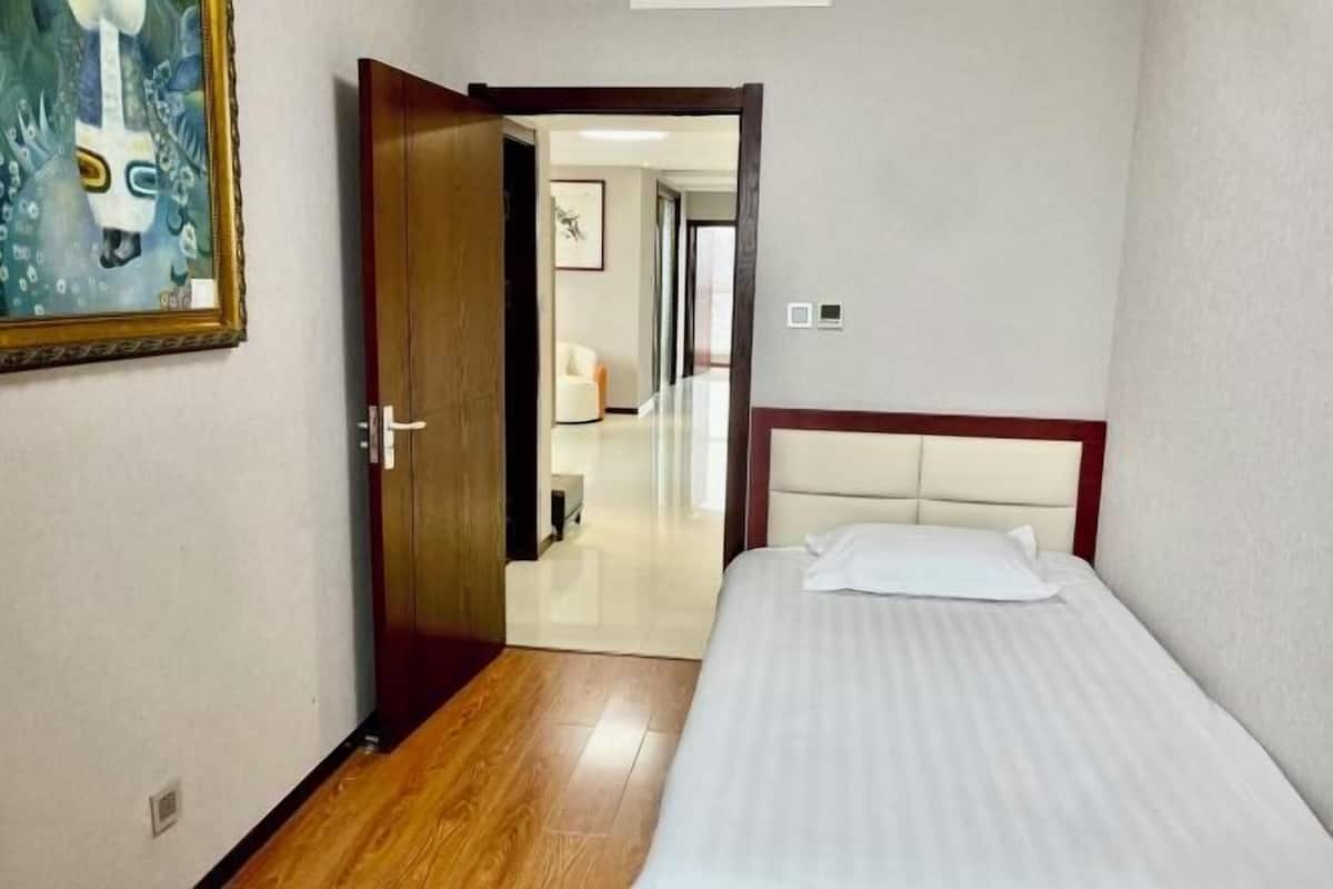 A hotel room with a bed, a door, and a hallway leading to another room.