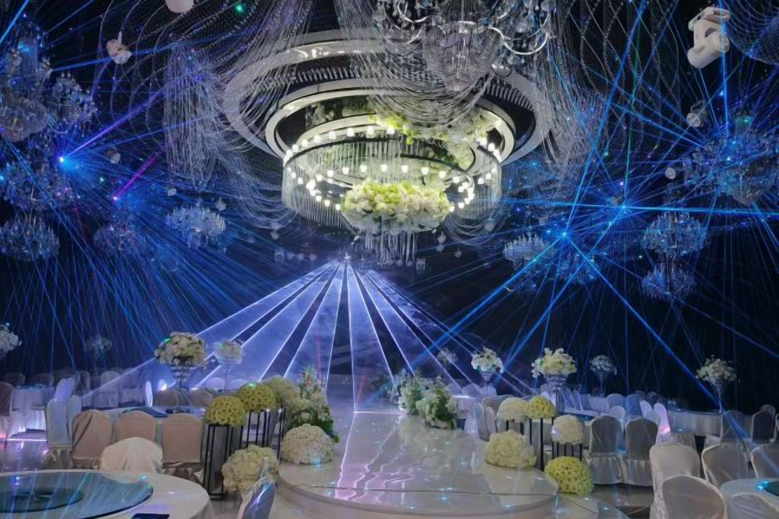 A venue with a central chandelier, tables with floral centerpieces, and a ceiling adorned with hanging lights.