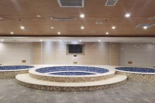 Un hall de hotel con una zona de estar central, un televisor de pantalla plana en la pared y suelo de baldosas.