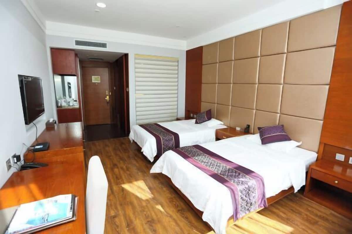 A hotel room with two beds, a wooden desk, a television, and a large padded headboard.