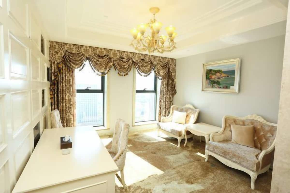 A room with a white desk, two chairs, a sofa, a chandelier, and a painting on the wall.