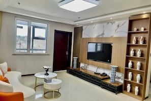 A modern living room with a large TV, comfortable seating, and decorative vases. - Guanlan International Hotel (Weihai)