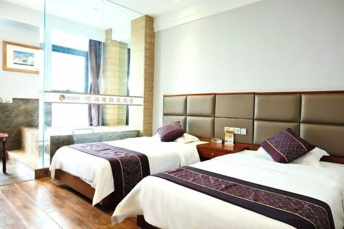 A hotel room with two beds, a large window, and a view of the outside.