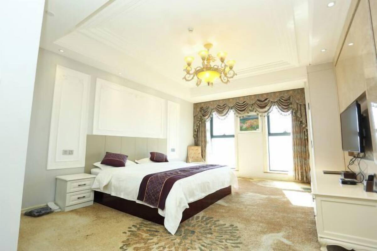 A spacious bedroom with a large bed, a chandelier, a television, and a view of the outdoors.
