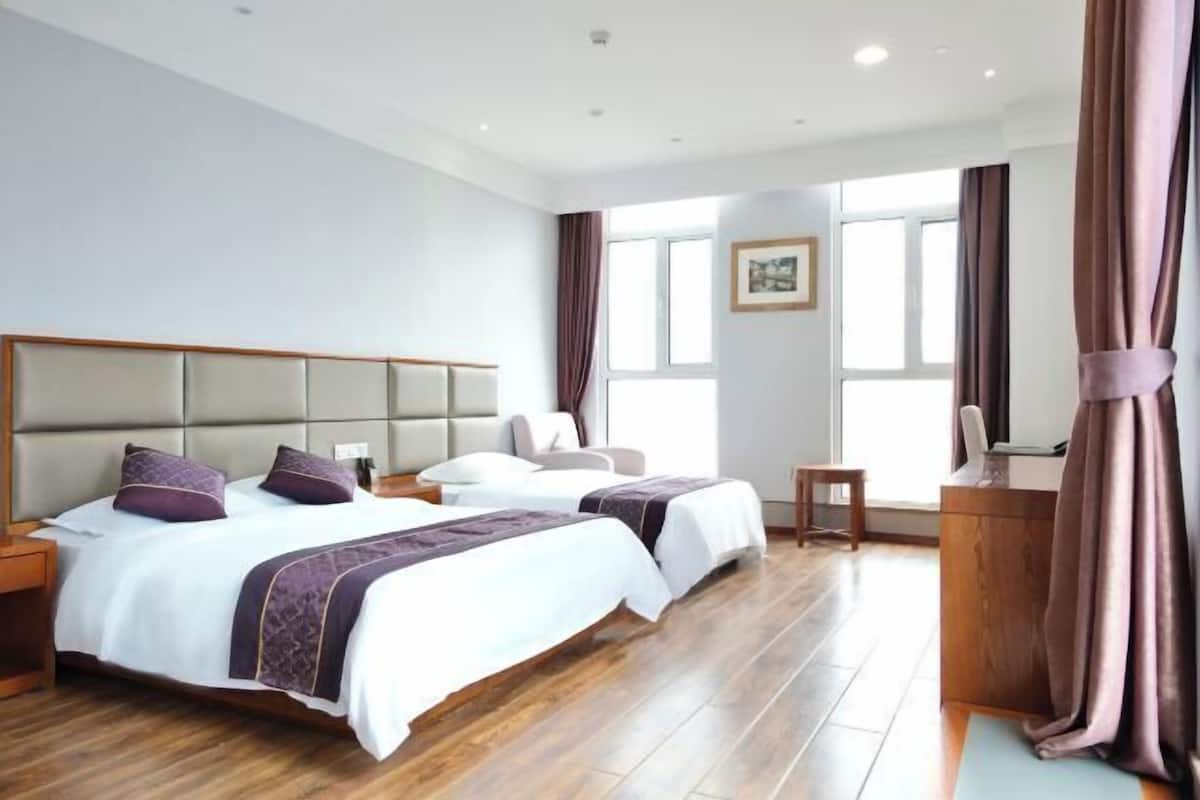 A hotel room with two beds, a desk, a chair, and a view of the outside.