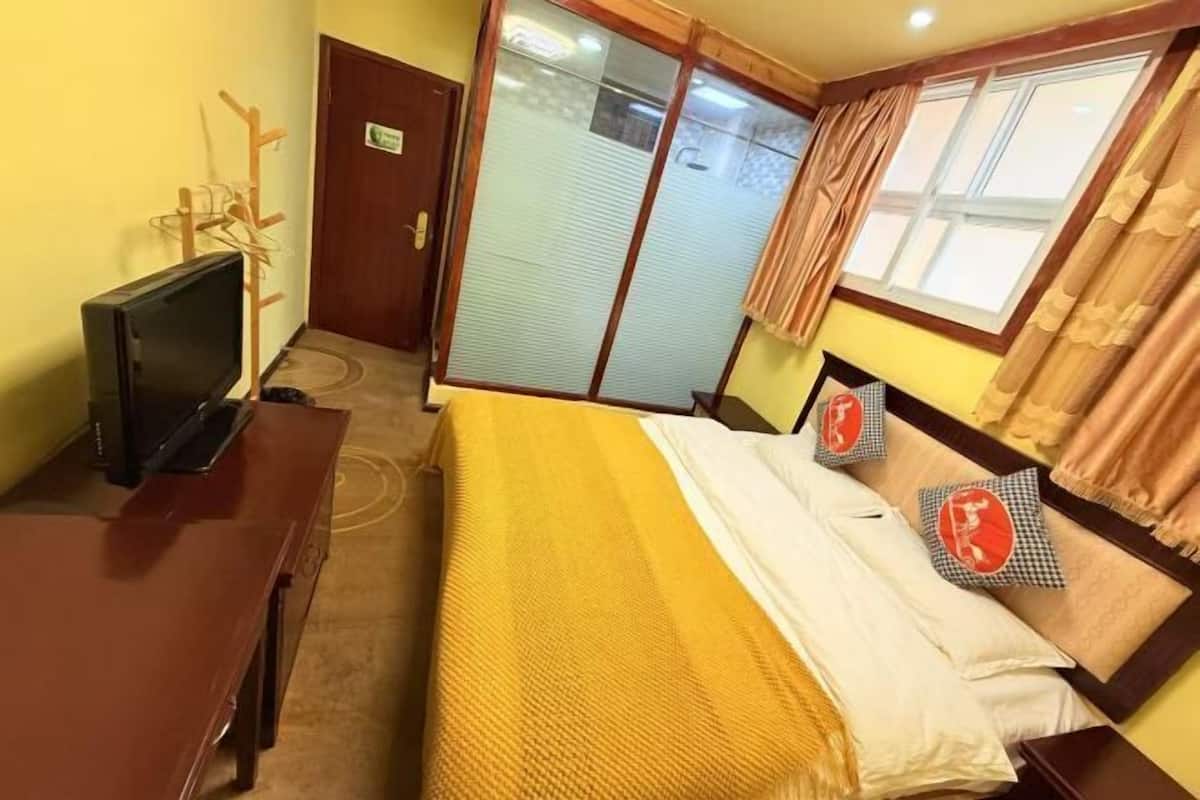 Ein Hotelzimmer mit Bett, Fernseher, Schreibtisch aus Holz, Kleiderschrank und einem Fenster mit Vorhängen.