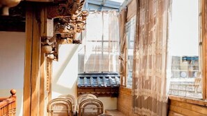 A narrow corridor with wooden carvings, a traditional tiled roof, and a view through a window with a curtain.