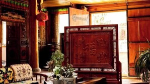 A traditional wooden interior with ornate carvings, a large wooden screen with Chinese characters, and a potted plant.