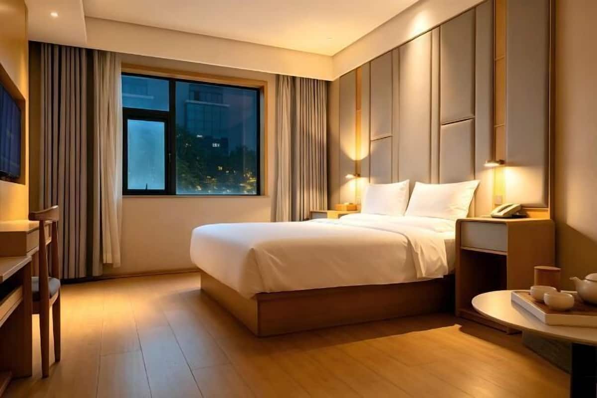 A hotel room with a large bed, bedside tables, a desk, a window with curtains, and a nightstand with a lamp.