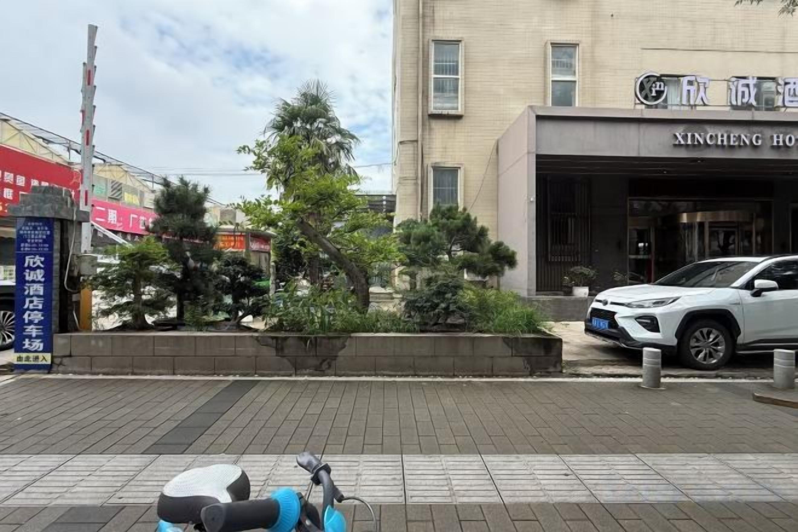Ingresso di un hotel con vialetto lastricato, un'auto parcheggiata e un edificio con insegne.