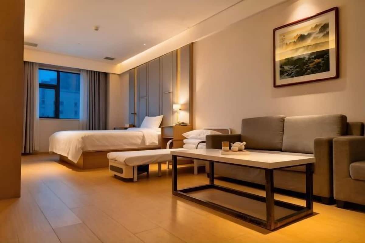 A hotel room with a bed, a sofa, a table, and a painting on the wall.