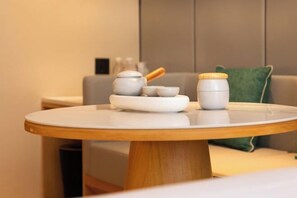 Uma mesa redonda de madeira com superfície branca, uma chaleira branca, uma xícara branca e um recipiente branco com tampa de madeira.