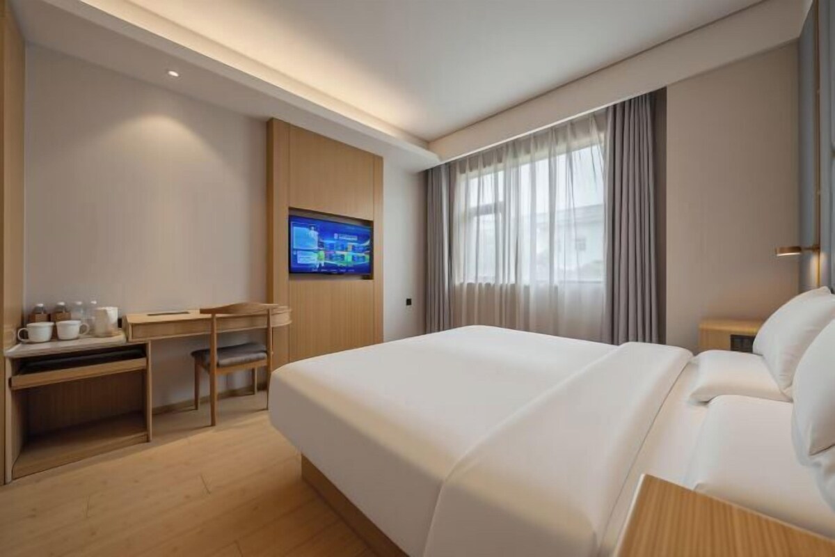 A hotel room with a bed, a desk, a TV, and a window with curtains.