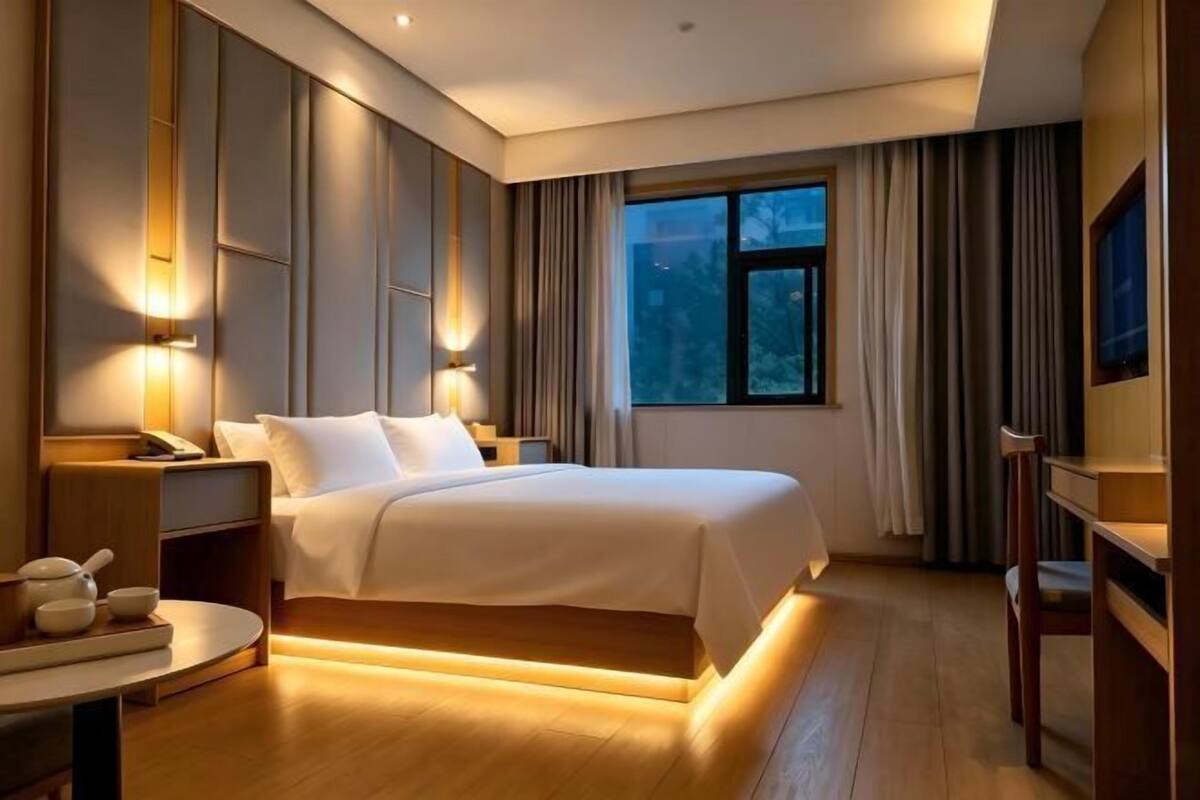 A hotel room with a large bed, bedside tables, a desk, and a window with curtains.