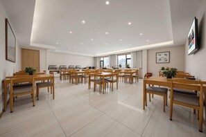 A spacious dining area with multiple wooden tables and chairs, a kitchen in the background, and large windows allowing natural light. - Xincheng Hotel (Xi'an Mingguang Road Bachengmen Subway Station) (Xi'an)