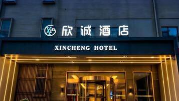 The exterior of the Xincheng Hotel with a modern facade, illuminated entrance, and signage in both Chinese and English.