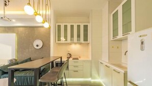 Une cuisine compacte avec des meubles blancs, un coin repas comprenant une table et des chaises, et un luminaire suspendu moderne.