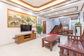 A living room with a television, wooden furniture, a staircase, and a large painting on the wall. - Zhouzhuang yijingbieyuan hotel (Kunshan)