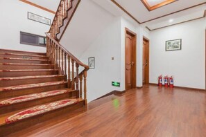 A wooden staircase with a patterned carpet, a fire extinguisher, and a door in a hallway with white walls and a wooden floor. - Zhouzhuang yijingbieyuan hotel (Kunshan)