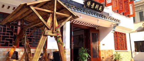 Un edificio tradizionale cinese con struttura in legno, un tendone rosso e un cartello con caratteri cinesi.