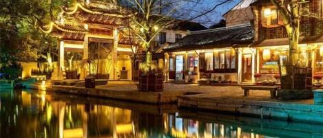 A traditional building with a reflection in the water, a pathway, and a small bridge.