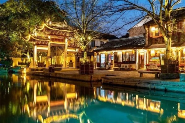 A traditional building with a reflection in the water, a pathway, and a small bridge.