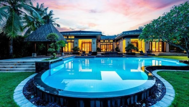 Un resort moderno con una amplia piscina circular, palmeras y un cielo al atardecer.