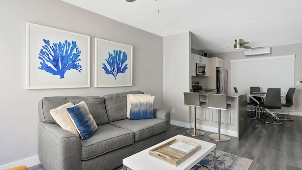 A modern living room with a grey sofa, two blue artwork pieces, a white coffee table, and a dining area with a bar and chairs. - ULTRA Modern Apt by the Beach (Hollywood)
