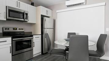 A modern kitchen with stainless steel appliances, a dining area with a round table and four chairs, and an air conditioning unit mounted on the wall.