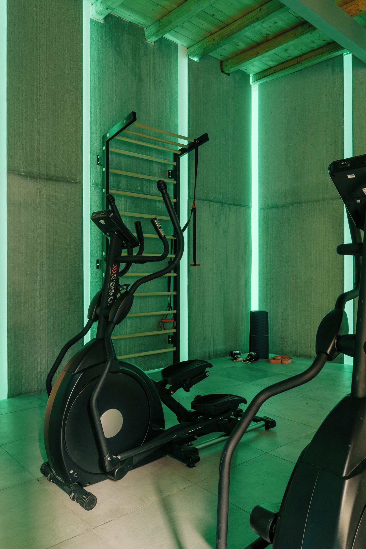 Een sportschool met trainingsapparatuur, waaronder een loopband en een hometrainer, plus een rek met gewichten.