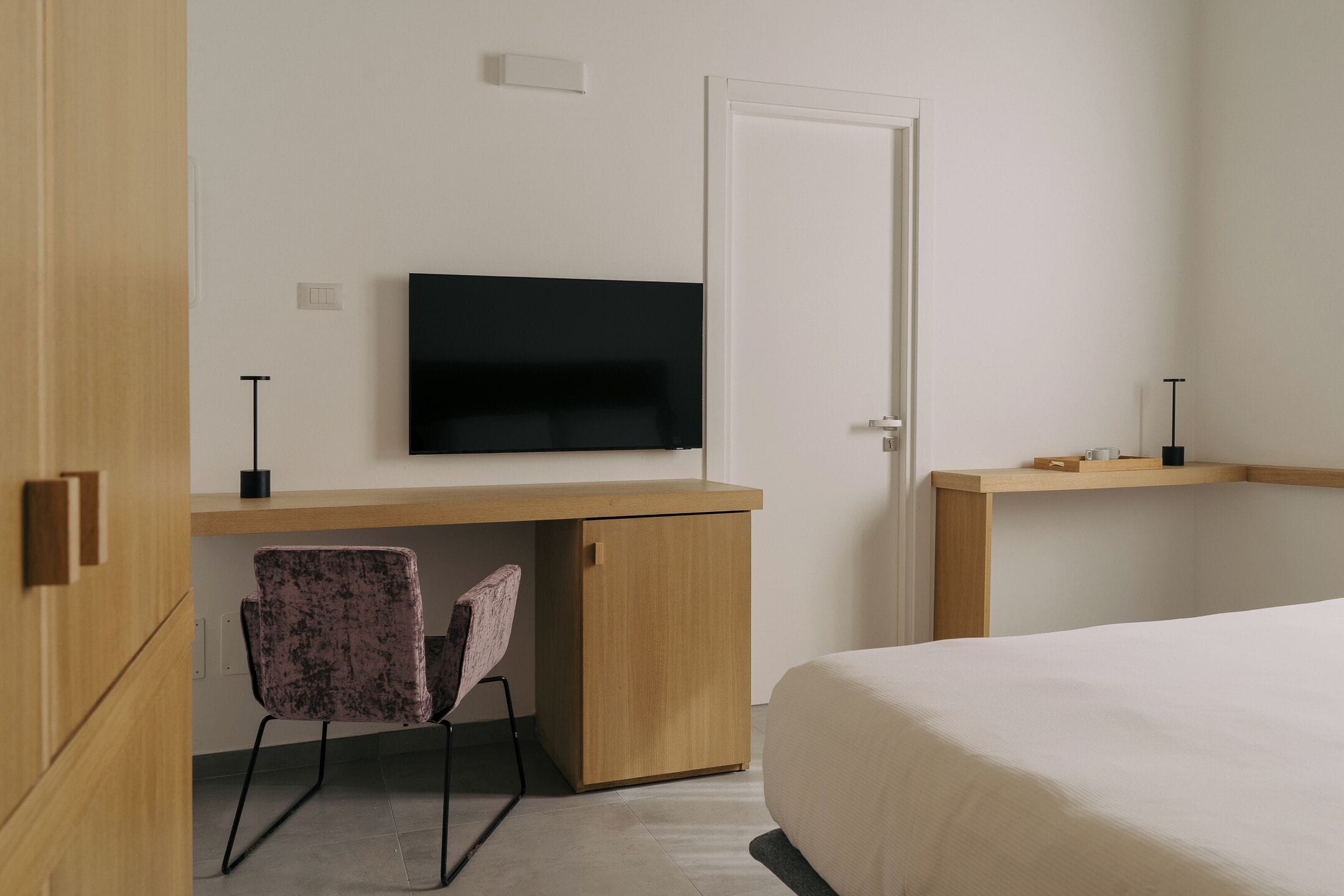 Una camera d'albergo con una scrivania in legno, una televisione a parete, una sedia e un letto.
