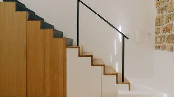 Un escalier avec des marches en bois et des rampes en métal noir, menant à un palier avec un mur blanc et une section de mur en pierre.