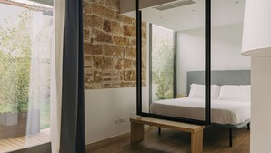 A modern bedroom with a large window, a wooden bench, and a bed with white linens. - Spasimo Hôtellerie (Palermo)