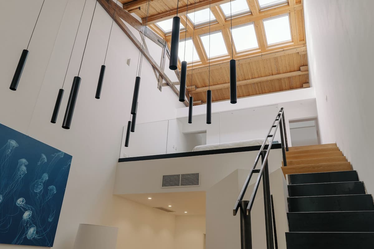 Ein modernes Interieur mit Treppe, Holzbalken und Pendelleuchten.