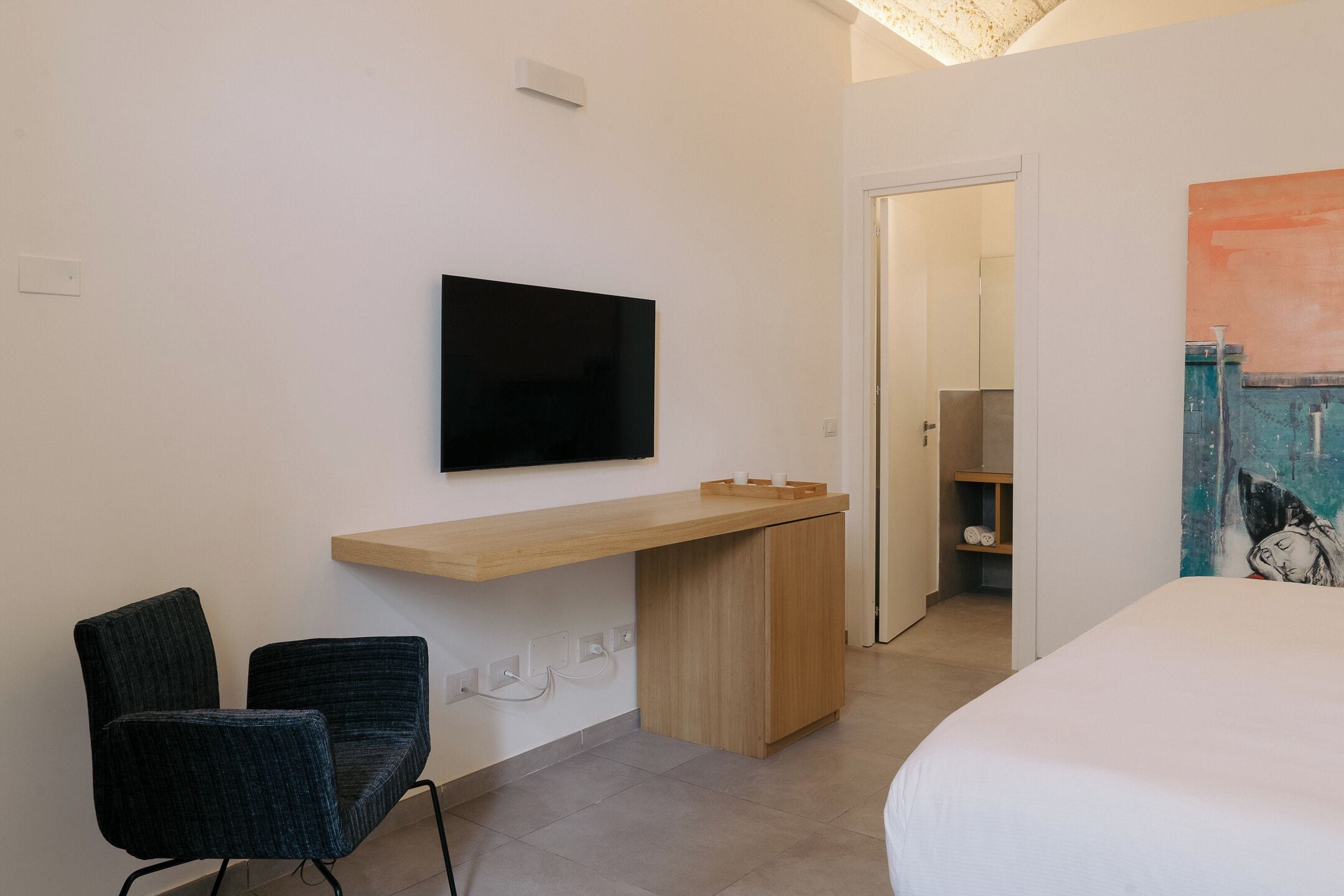 Una habitación de hotel moderna con una cama, un escritorio con televisor de pantalla plana, dos sillas y un cuadro en la pared.