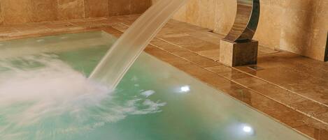 Un espacio de spa con fuente de agua, paredes de piedra y suelo de baldosas.