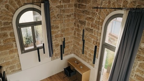 A room with a wooden desk, two windows with curtains, and a stone wall. - Spasimo Hôtellerie (Palermo)