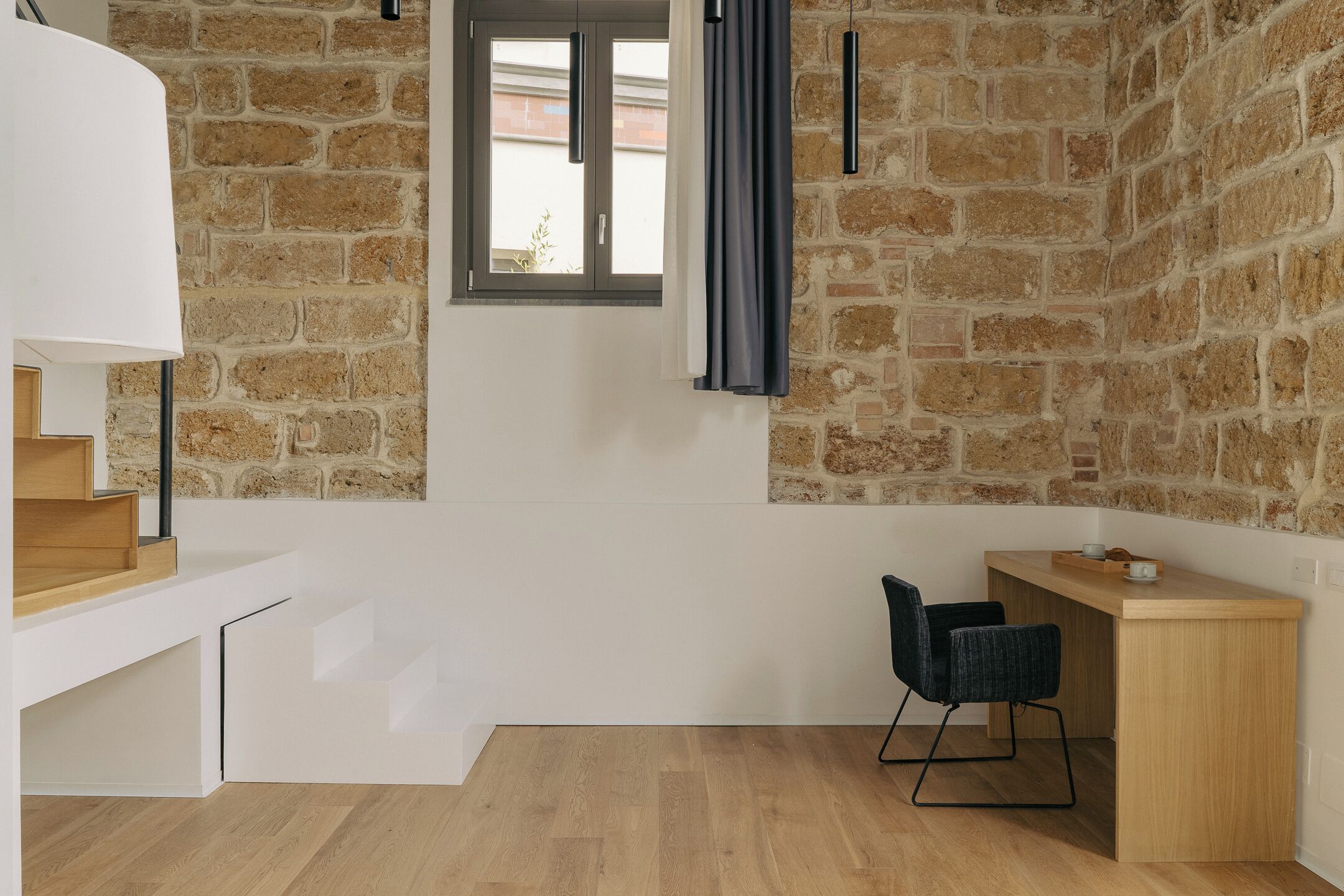 Une pièce moderne avec un mur en pierre, un bureau en bois, une chaise et un escalier blanc.