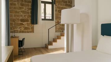 A bedroom with a large bed, a desk with a chair, a staircase, and a window with curtains.