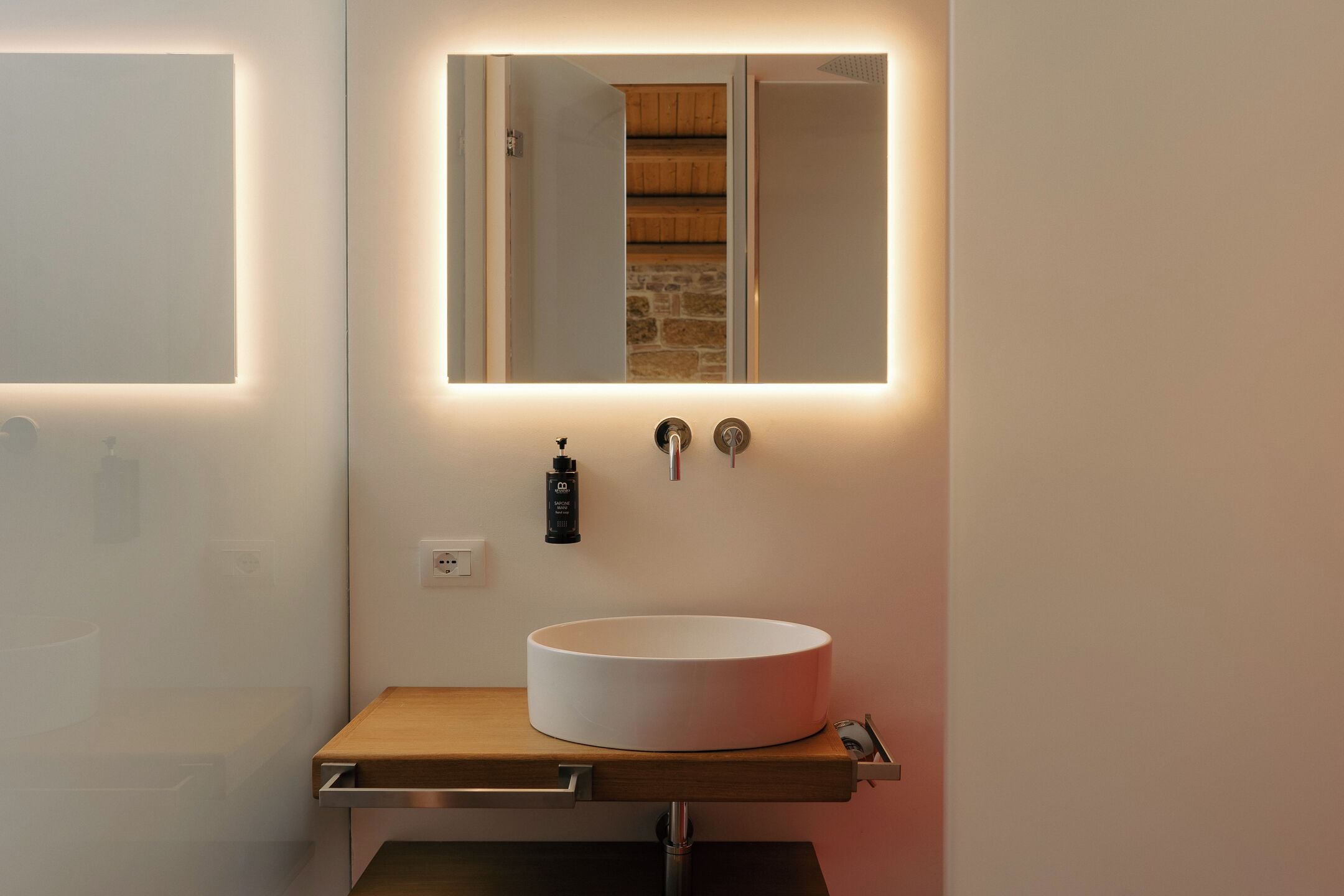 Un bagno con un lavandino bianco rotondo, uno specchio e un piano di lavoro in legno.
