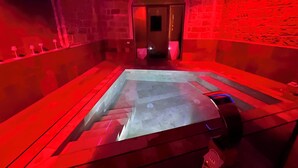 A spa room with a glass-enclosed hot tub, stone walls, and red ambient lighting. - Spasimo Hôtellerie (Palermo)