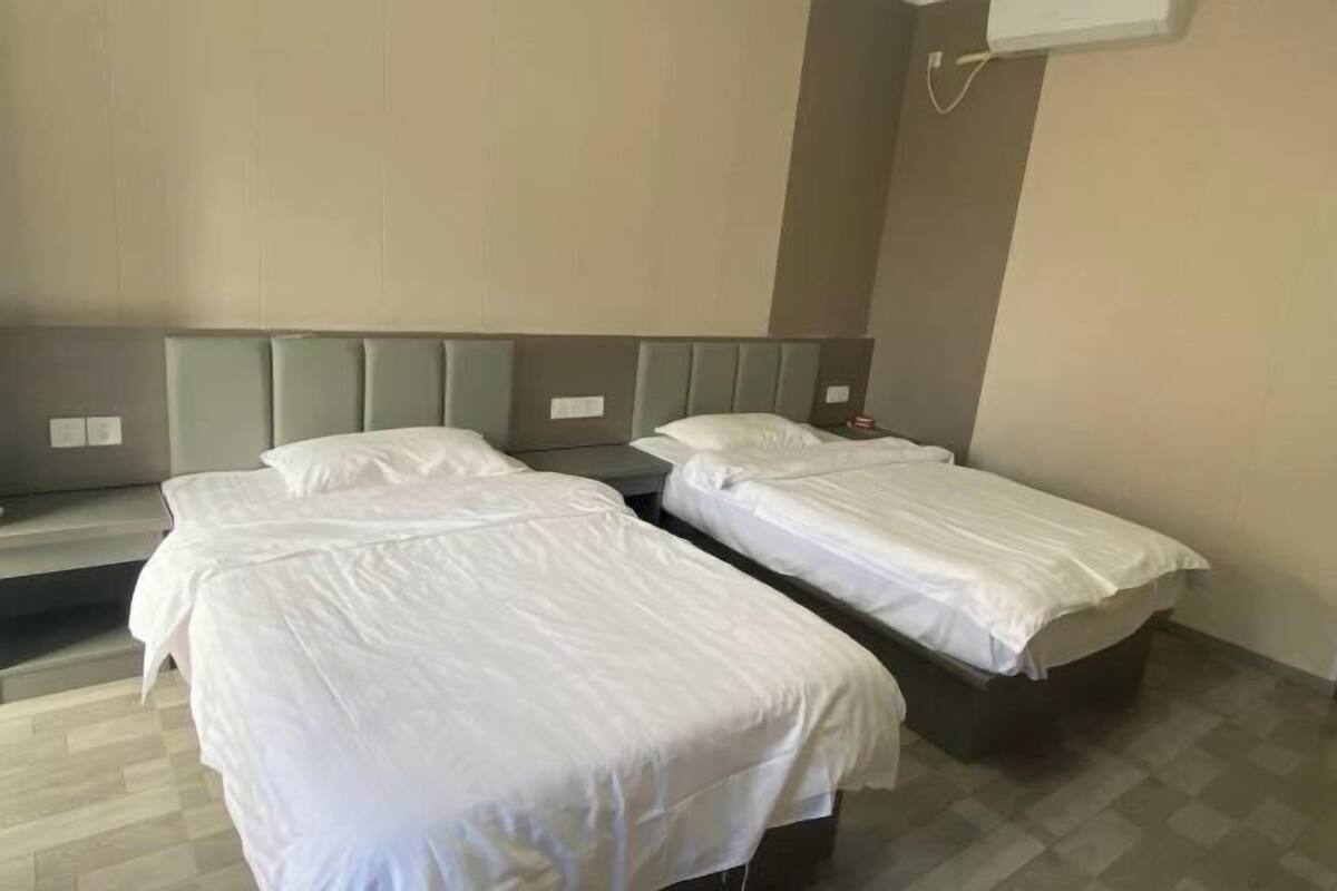 Una habitación de hotel con dos camas individuales, un banco y un aire acondicionado instalado en la pared.