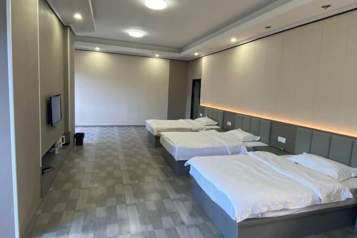 Una habitación de hotel con tres camas, un televisor en la pared y un mostrador de recepción.