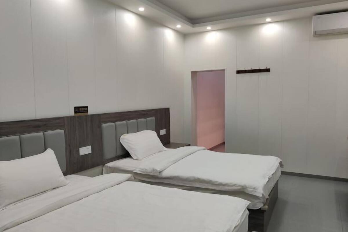 Habitación de hotel con dos camas, cabecera de madera, mesita de noche pequeña y puerta rosa.