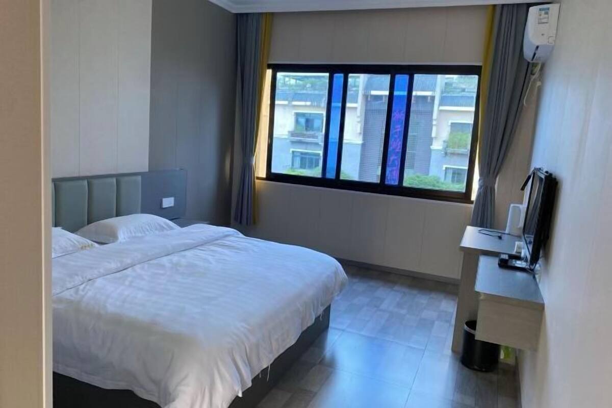 Una habitación de hotel con cama, escritorio, ventana con cortinas y vistas a edificios.