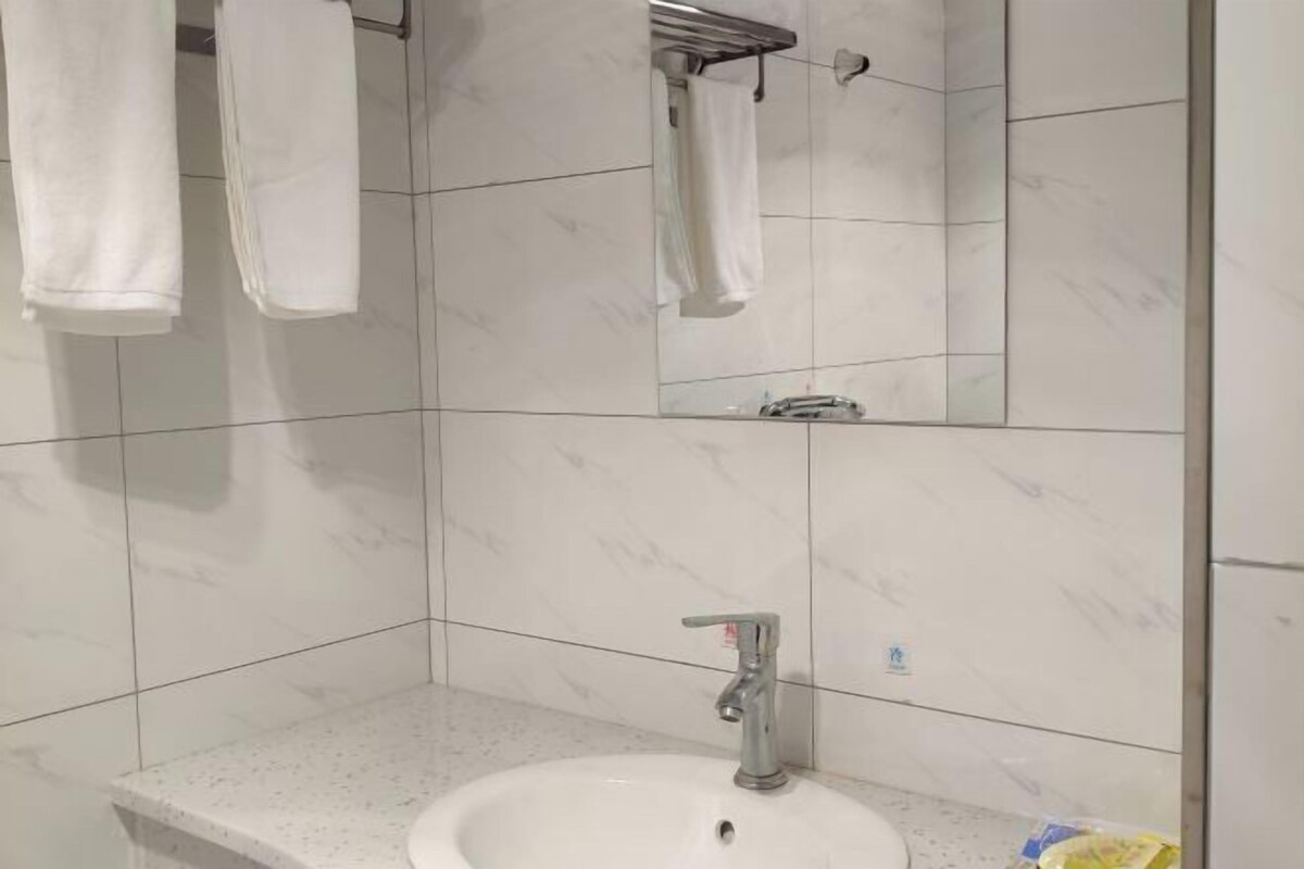 Une salle de bain carrelée de marbre blanc, avec un lavabo doté d’un robinet et deux serviettes suspendues à des crochets.
