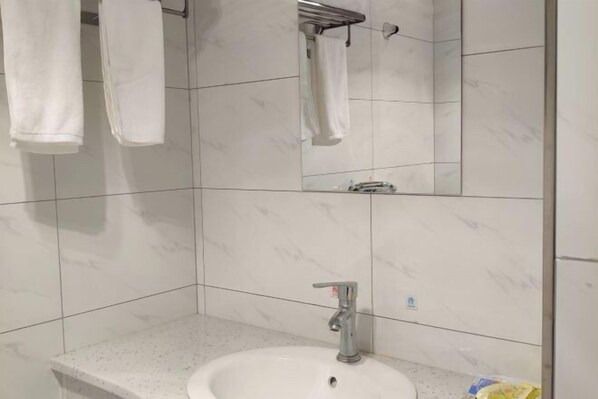 Une salle de bain carrelée de marbre blanc, avec un lavabo doté d’un robinet et deux serviettes suspendues à des crochets.