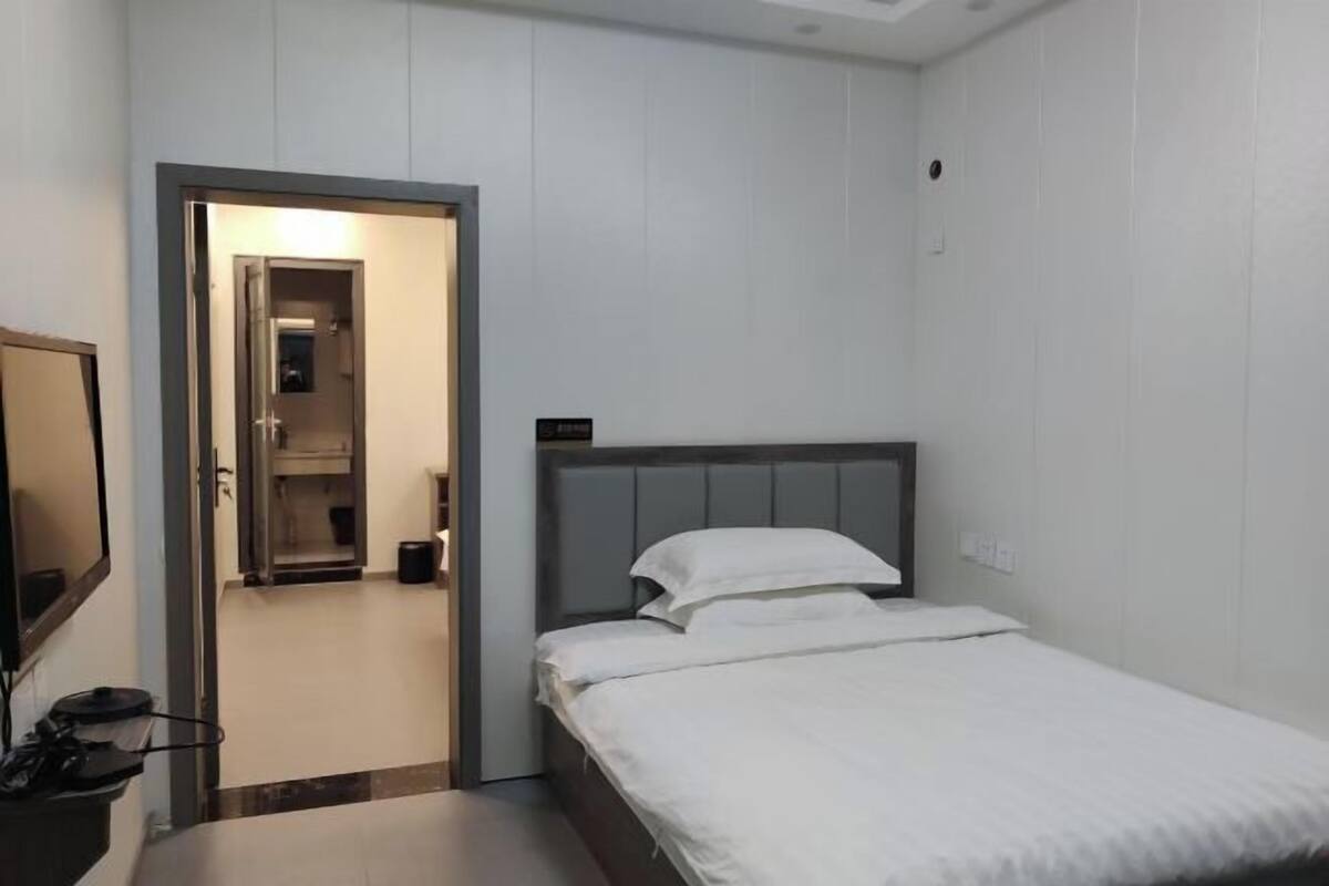 Una habitación de hotel pequeña y moderna con una cama individual, televisión y puerta que da al baño.